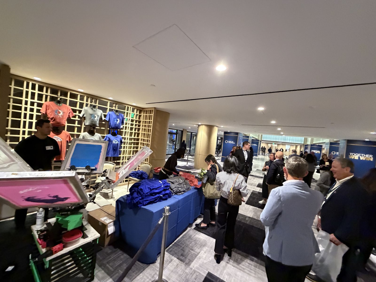 Live apparel personalization station serving a line of attendees in a conference center corridor