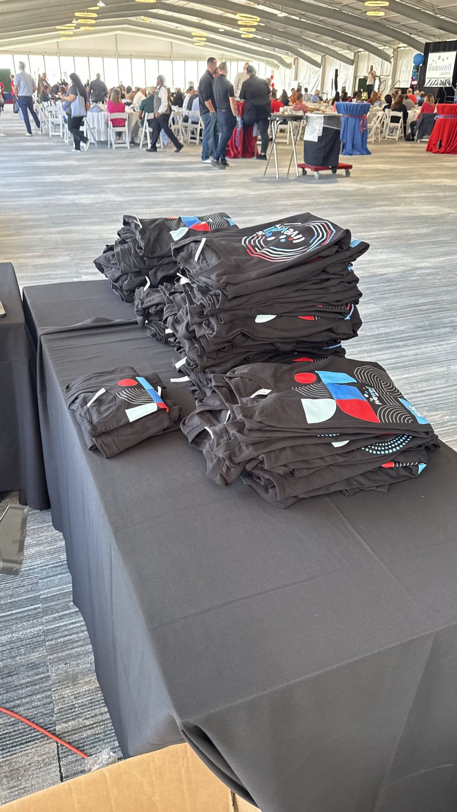 Stacks of folded event shirts arranged on a black-linen table inside a large gala tent