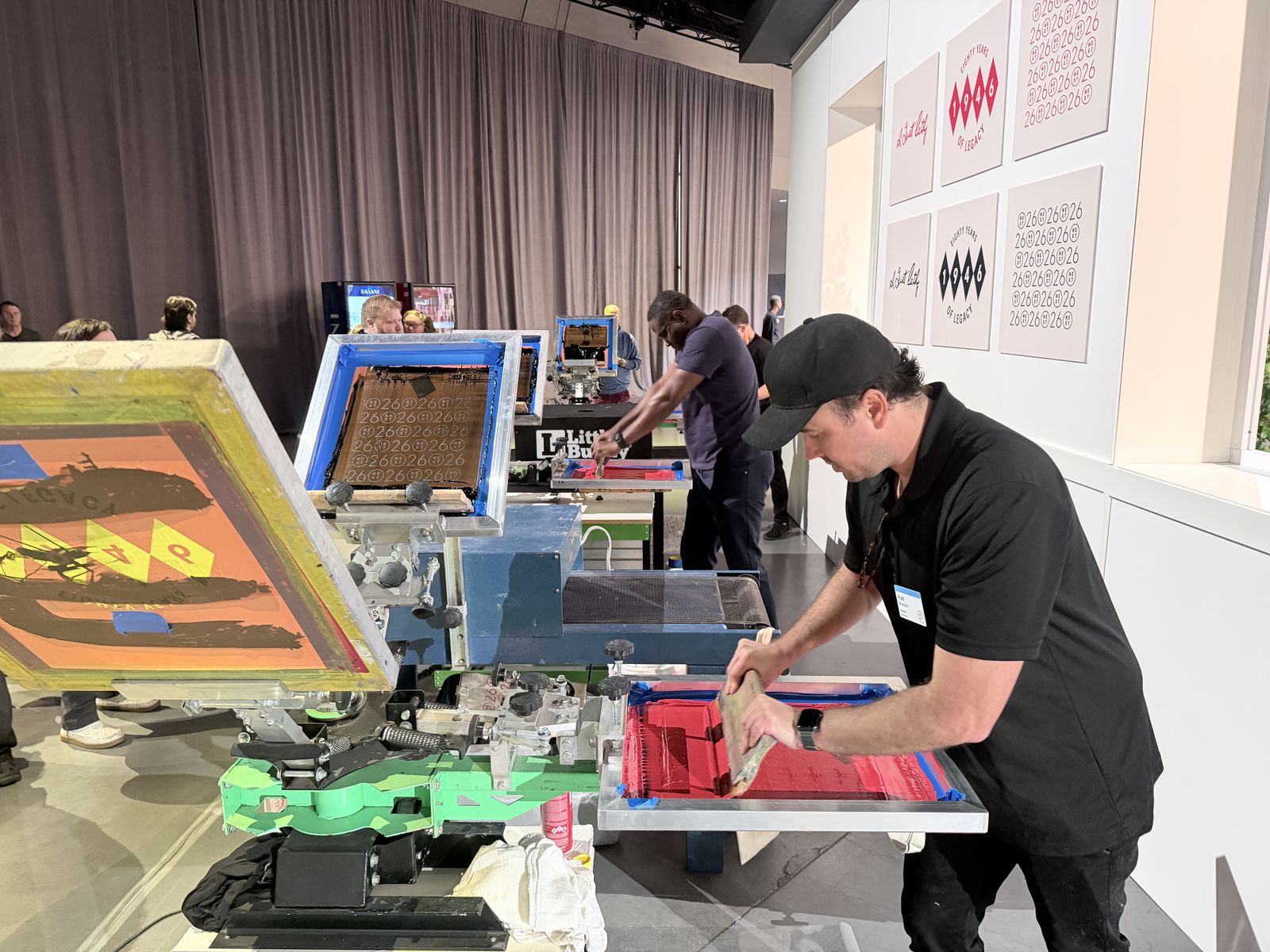 Merch Troop crew running side-by-side live printing stations at a brand activation with artwork panels on the wall